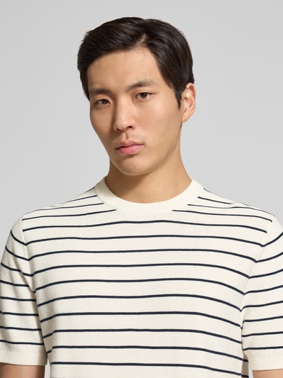 Männermodel trägt Strickshirt mit geripptem Rundhalsausschnitt von MCNEAL aus Reine gewachste Baumwolle, Nahaufnahme Oberkörper.