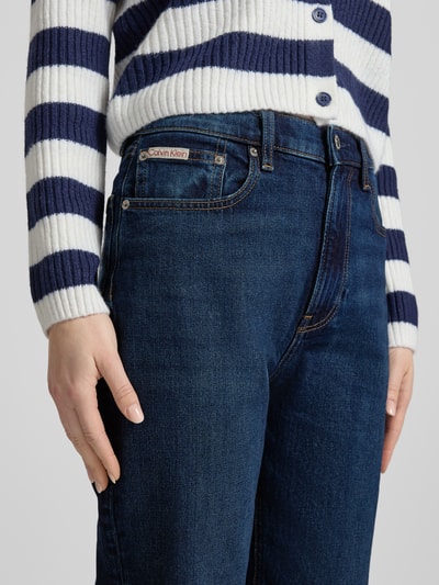 Kobieta nosi Straight Fit Jeans mit Logo-Patch Modell 'New Moon' od Calvin Klein Jeans, elastyczna mieszanka bawełny, 5 kieszeni, kolor ciemnoniebieski, szerokość w rozmiarze 27/32: 35 cm, długość nogawki: 77 cm, zapięcie na guzik i zamek, zbliżenie na górną część ciała.