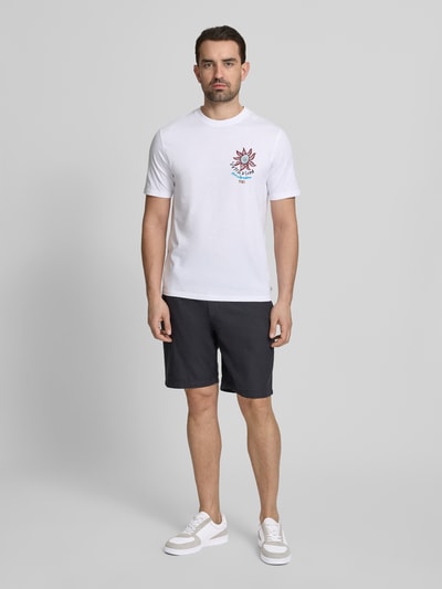 Männermodel trägt T-Shirt mit Label-Print und Rundhalsausschnitt von Scotch & Soda in Weiß, Reine Baumwolle, Regular-Fit, Rückenlänge 70 cm, Ganzkörperansicht von vorne.
