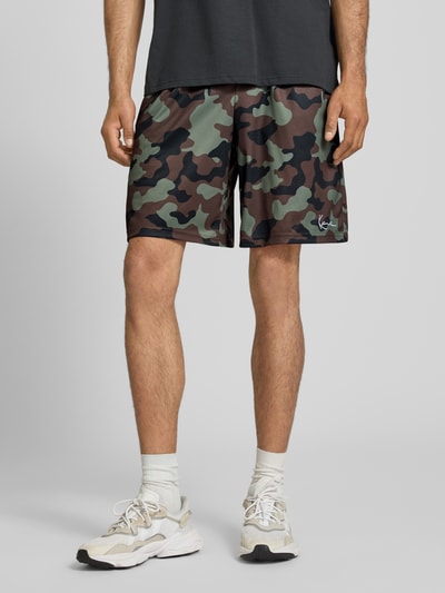 Männermodel trägt Regular Fit Shorts mit elastischem Bund von KARL KANI mit Camouflage-Strukturmuster und Logo-Stitching, Nahaufnahme Unterkörper.
