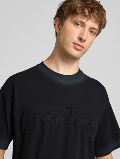 Męski model nosi T-Shirt mit Label-Stitching und Rundhalsausschnitt od ANOTHER COTTON LAB, bawełna, krój relaxed fit, długość tyłu 67 cm, zbliżenie na górną część tułowia.
