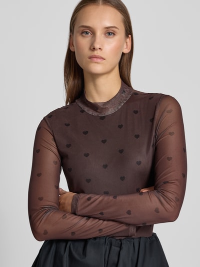 Modelka nosi Slim Fit Langarmshirt mit Allover-Muster Modell 'ERICA' von ONLY, ciemnobrązowa siateczka z czarnymi sercami, krój slim fit, wysokozabudowany dekolt, długie rękawy, materiał mesh, widok z przodu, zbliżenie na górną część ciała.