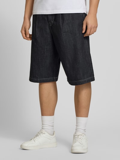 Mężczyzna nosi Extra Baggy Fit bermudy model LLOYD od Jack & Jones, ciemnoniebieska bawełna, wpuszczane kieszenie, szerokość w rozmiarze M: 41 cm, długość wewnętrzna nogawki w rozmiarze M: 30 cm, widok z przodu na całe ciało.