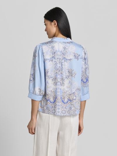 Frauenmodel trägt Regular-Fit Damen Bluse mit Allover-Look und Paisley-Muster, Stehkragen, V-Ausschnitt, Knopfleiste, 3/4-Arm, Modell 'Roselle Artist Paisley' von Neo Noir, Rückenlänge 57 cm, Ärmellänge 43 cm, helle Blautöne mit beigen und weißen Akzenten, geschmeidige Textur, Ganzkörperansicht Rückansicht.