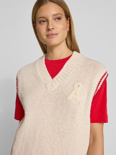 Vrouwenmodel draagt Loose Fit spencer van katoenmix model 'ICONIC A COLLEGE' van Armedangels, effen gebreide look met gestikt logo, contraststrepen, v-hals, geribde rompzoom, detailopname bovenlichaam.