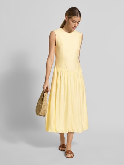 Modelka nosi żółtą sukienkę Bubble Kleid mit Rundhalsausschnitt Modell 'KRISSI' od YAS z lyocellem, krój slim fit, midi, gładka tekstura, lekko rozkloszowany dół, z tyłu zamek, długość pleców w rozmiarze 36: 45 cm, szerokość w rozmiarze 36: 43 cm, całkowity widok z przodu