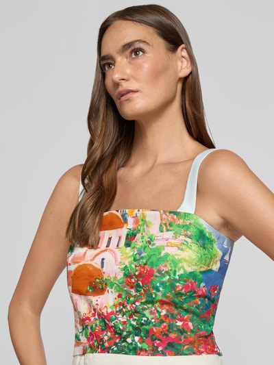 Frauenmodel trägt Cropped Blusentop mit Smok-Details von Stefanel in buntem Allover-Look aus Reiner Baumwolle, Nahaufnahme Oberkörper. Rückenlänge bei Größe S: 21 cm.