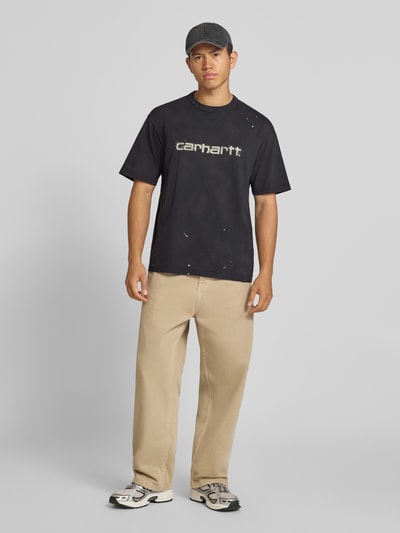 Męski model nosi czarny t-shirt Regular Fit z bawełny Model 'Painter' od Carhartt Work In Progress, detal z logo, Długość tyłu w rozmiarze M: 72 cm, zdjęcie całej sylwetki z przodu.