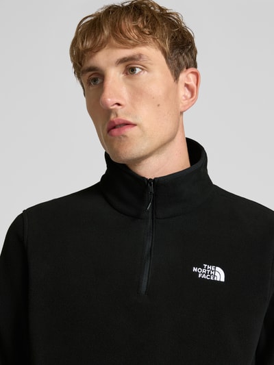 Męski model nosi Fleecepullover mit Troyer-Kragen Modell 'GLACIER' od The North Face, czarny, wyhaftowane logo, prosty krój, zbliżenie na górną część ciała.