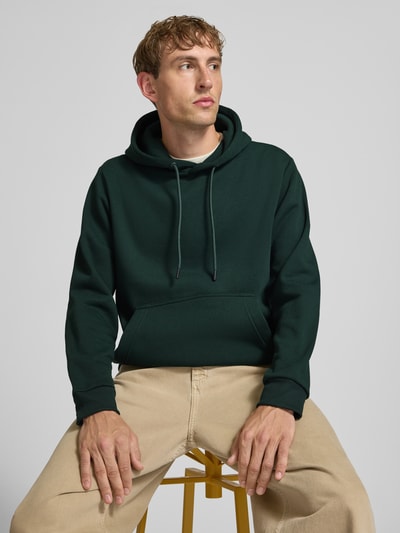 Männermodel trägt Hoodie mit Känguru-Tasche Modell 'BRADLEY' von JACK & JONES in Dunkelgrün, lockerer Schnitt, Nahaufnahme Oberkörper.