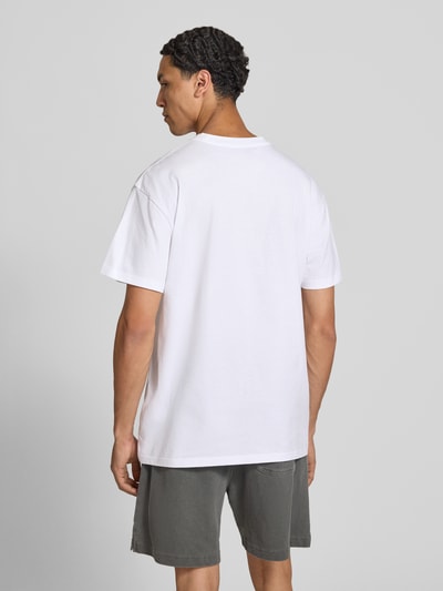 Männermodel trägt T-Shirt mit Logo-Stitching Modell 'Gracious' von Carhartt Work In Progress, weiß, Baumwolle, Ganzkörperansicht Rückansicht.