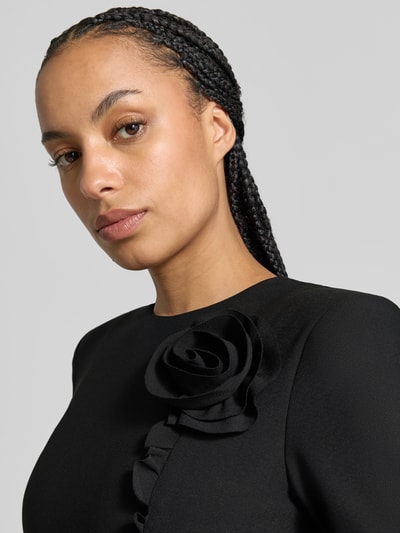 Frauenmodel trägt Slim Fit Minikleid mit floralem Besatz von ROTATE, schwarzer elastischer Stoff, Rundhalsausschnitt, Nahaufnahme Oberkörper.