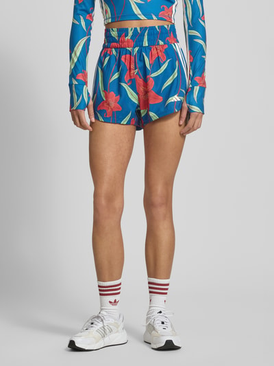 Frauenmodel trägt Regular Fit Shorts mit Allover-Muster von adidas Sportswear in Blau mit floralem Print, elastischer Bund, seitliche Eingrifftaschen, Ganzkörperansicht von vorne