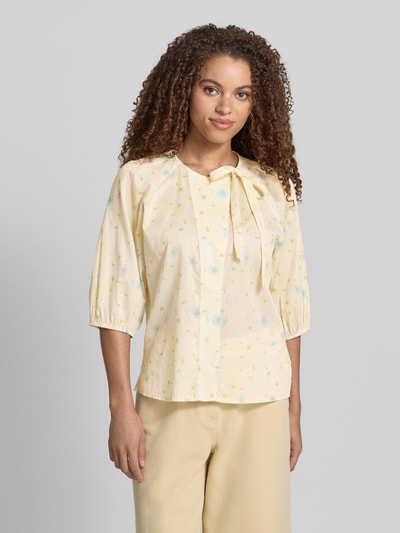 Frauenmodel trägt Bluse mit Rundhalsausschnitt und Binde-Detail von JAKE*S STUDIO WOMAN aus reiner Baumwolle, ganzkörperansicht von vorne. Gerader Schnitt, verdeckte Knopfleiste, 3/4-Arm, zarte Gelbtöne mit pastellfarbenem Print, Rückenlänge 59 cm, Ärmellänge 48 cm.