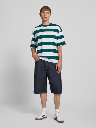 Männermodel trägt T-Shirt mit Label-Stitching und Rundhalsausschnitt von REVIEW, grün-weiß gestreift, Relaxed-Fit, Reine Baumwolle, Allover-Look, Rückenlänge bei Größe M 67 cm, Ganzkörperansicht von vorne.