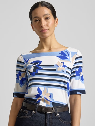 Kobiece modelka nosi T-shirt aus Viskose-Mix mit Rundhalsausschnitt von Betty Barclay, mieszanka wiskozy i elastanu, taliowany krój, okrągły dekolt, rękaw o dł. 1/2, długość tyłu w rozmiarze 36: 59 cm, niebieskie, białe i beżowe kwiaty oraz paski, wyraźna faktura materiału, zbliżenie na górną część ciała.