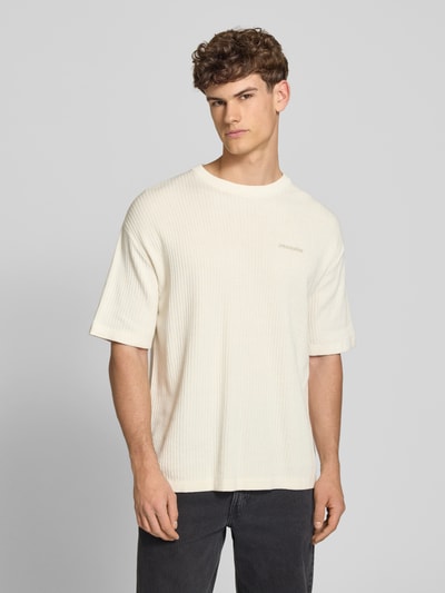 Męski model nosi Strickshirt mit Strukturmuster und Label-Stitching von Pegador z bawełny, krój relaxed fit, okrągły dekolt, długość tyłu 71 cm, fakturowany wzór, wyhaftowane logo, widok z przodu, ujęcie do pasa.