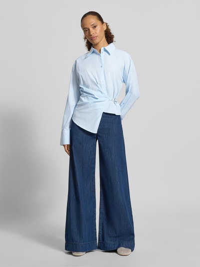 Frauenmodel trägt Regular Fit Hemdbluse aus reiner Baumwolle Modell 'Bella' von My Essential Wardrobe, hellblauer Stoff, Hemdblusenkragen, langärmelig, Zierbesatz, kombiniert mit weiter Jeanshose, Ganzkörperansicht von vorne.