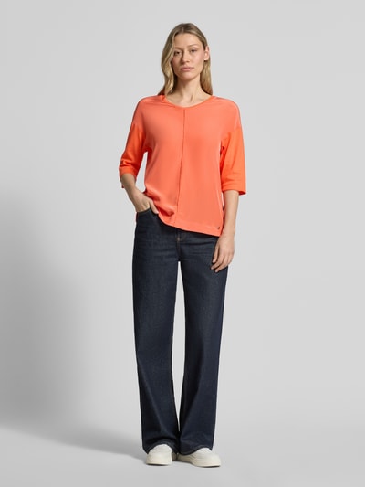 Frauenmodel trägt damski t-shirt mit Label-Detail von Marc Cain, mieszanka bawełny i elastanu, prosty krój, dekolt w serek, ozdobne szwy, rękaw o dł. 3/4, długość tyłu 60 cm w rozmiarze 36, kolor koralowy, gładka faktura, Ganzkörperansicht von vorne.