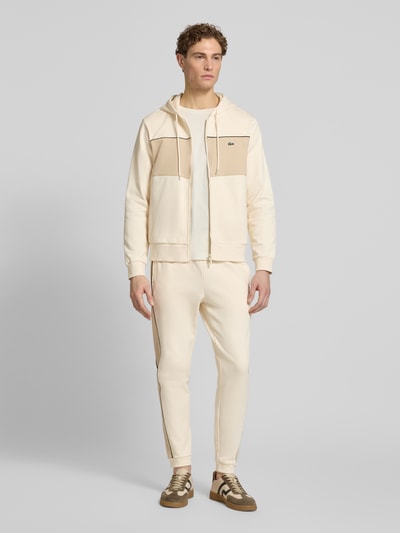 Männermodel trägt Regular Fit Sweatjacke aus reiner Baumwolle von Lacoste in Unifarben Two Tone mit Kontraststreifen, Ganzkörperansicht von vorne.