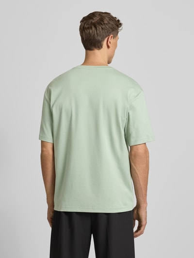 Männermodel trägt Relaxed Fit T-Shirt aus reiner Baumwolle Modell 'JOIN' von BOSS Green in Hellgrün, Unifarbe, Kurzarm, Ganzkörperansicht Rückansicht