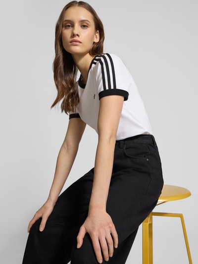 Frauenmodel trägt Slim Fit T-Shirt aus Baumwoll-Mix von adidas Originals in Weiß mit schwarzen Streifen, Rundhalsausschnitt, Nahaufnahme Oberkörper.