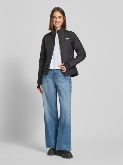 Frauenmodel trägt Steppjacke mit Logo Modell 'CANYONLANDS' von The North Face in Schwarz mit Stehkragen, Ganzkörperansicht von vorne.