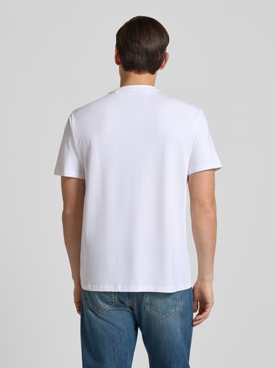 Männermodel trägt T-Shirt mit Logo und Rundhalsausschnitt von Guess in Weiß, Baumwoll-Mix mit Modal, Relaxed Fit, Ganzkörperansicht Rückansicht.