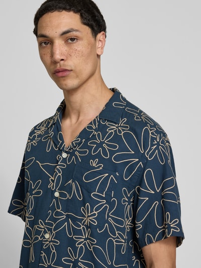 Männermodel trägt Freizeithemd mit Reverskragen von Forét, blauer Baumwoll-Mix mit floralen Stickereien, Regular Fit, Nahaufnahme Oberkörper.