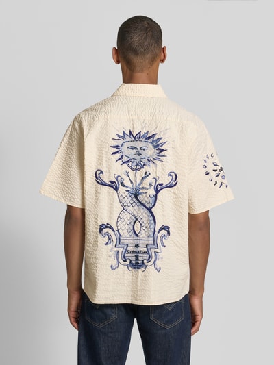 Männermodel trägt Relaxed Fit Freizeithemd aus reiner Baumwolle von Scotch & Soda in Beige mit Strukturmuster und blauem Motiv-Stitching, Ganzkörperansicht Rückansicht.
