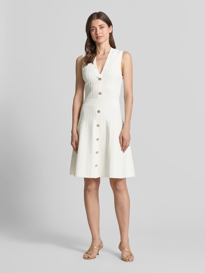 Frauenmodel trägt Knielanges Kleid aus Viskose-Mix Modell 'Amber' von Guess in Strick-Optik, taillierter Passform, Ärmelloses-Design, V-Ausschnitt, Knielänge, Farbe Offwhite, Ganzkörperansicht von vorne.