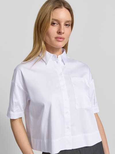 Frauenmodel trägt Hemdbluse mit Brusttasche und Kentkragen von More & More, weiß, Baumwoll-Mix mit Stretch-Anteil, Regular-Fit, Knopfleiste, leicht überschnittene Schultern, Nahaufnahme Oberkörper.