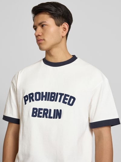 Männermodel trägt T-Shirt mit Label-Stitching Modell 'Rush' von PROHIBITED in Weiß mit dunkelblauen Details, Nahaufnahme Oberkörper.