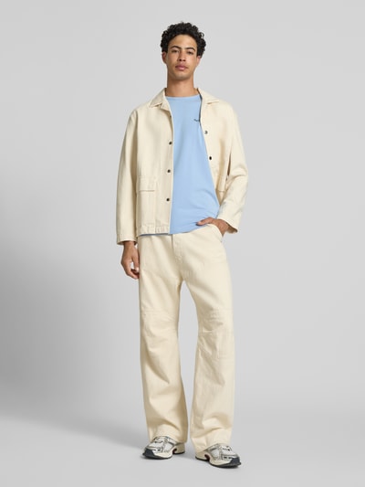 Männermodel trägt Slim Fit T-Shirt aus Baumwoll-Mix Modell 'ORIGINAL BASIC 3N' von Pepe Jeans, unifarben hellblau, Jerseytextur, Label Print, kurzarm, kombiniert mit cremefarbener Hose und Jacke, Ganzkörperansicht von vorne.