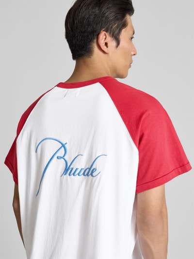 Männermodel trägt T-Shirt mit Label-Stitching von RHUDE in Weiß mit roten Ärmeln, Reine Baumwolle, Gerade Passform, Ganzkörperansicht Rückansicht.