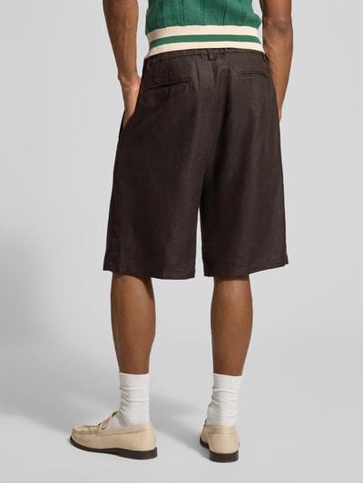 Mężczyznamodel nosi ciemnobrązowe Leinenshorts aus reinen Leinen von Drykorn, luźny krój, kieszenie, szerokość w rozmiarze 33: 44 cm, długość nogawki 25 cm, widok całej sylwetki z tyłu.