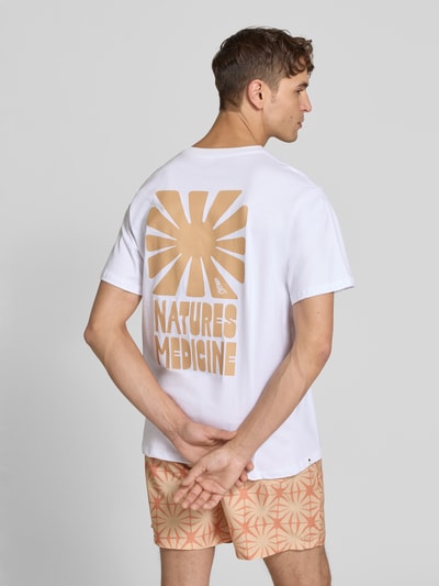 Männermodel trägt T-Shirt mit Label-Print und Rundhalsausschnitt von BOARDIES in Weiß mit beigem Print, Reine Baumwolle, Regular-Fit, Rückenlänge 73 cm bei Größe M, Ganzkörperansicht Rückansicht.