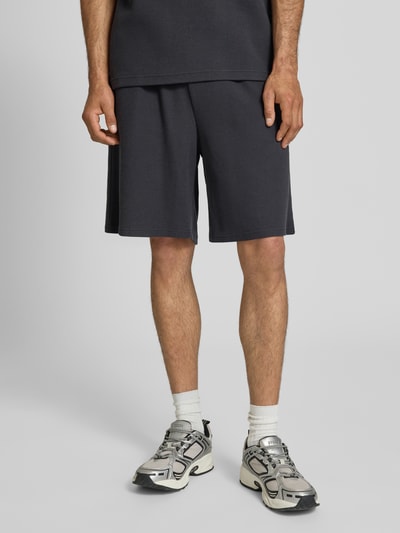 Männermodel trägt Relaxed Fit Shorts mit Strukturmuster von KARL KANI aus Baumwoll-Mix in Dunkelgrau, elastischer Bund, Nahaufnahme Unterkörper.