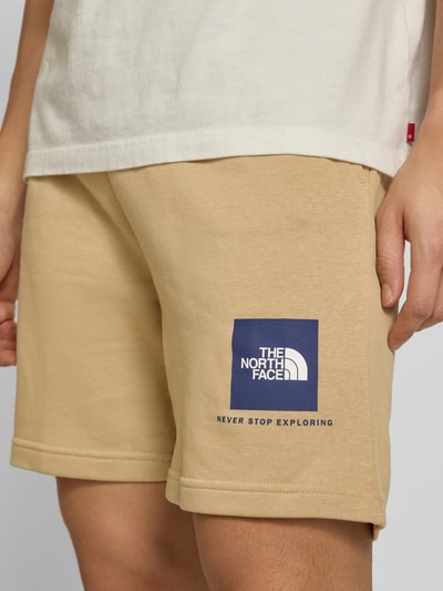 Mężczyznа nosi Regular Fit Shorts mit Eingrifftaschen von The North Face, mieszanka bawełny, wpuszczane kieszenie, szerokość w rozmiarze M: 40 cm, długość wewnętrzna nogawki: 18 cm, kolor beżowy, prosty krój, widoczne logo, nahaufnahme dolnej części ciała.