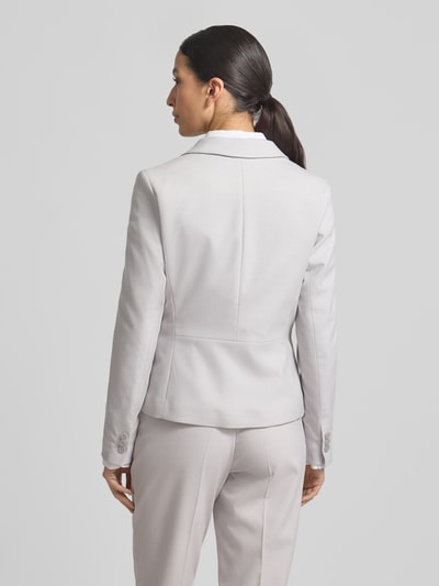 Modelka kobieca nosi Slim Fit Blazer mit Reverskragen od More & More, jasnoszary, materiał z domieszką wiskozy, krój slim fit, zapinany na guzik, kieszenie z lamówką, długość tyłu w rozmiarze 36: 57 cm, szerokość w rozmiarze 36: 46 cm, długość rękawa w rozmiarze 36: 64 cm, widok całej sylwetki z tyłu.