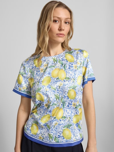 Vrouwenmodel draagt Blusenshirt aus Satin im Allover-Look van Christian Berg Woman, satijn, regular fit, all-over look, ronde hals, ruglengte bij maat 36: 56 cm, mouwlengte bij maat 36: 20 cm, kleurrijke citroenprint met blauwe details, vooraanzicht close-up.