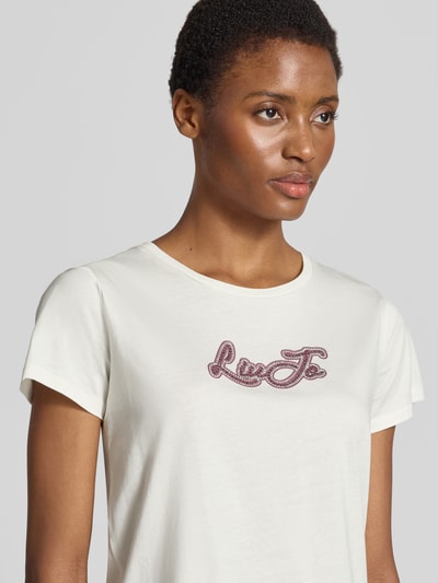 Frauenmodel trägt T-Shirt mit Strasssteinbesatz von Liu Jo in Weiß, reiner Baumwolle, gerader Schnitt, Nahaufnahme Oberkörper.