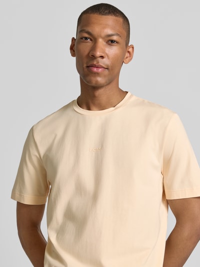 Männermodel trägt Regular Fit T-Shirt aus Baumwoll-Mix Modell 'TCHUP' von BOSS für BOSS Orange in hellem Beige, Nahaufnahme Oberkörper.
