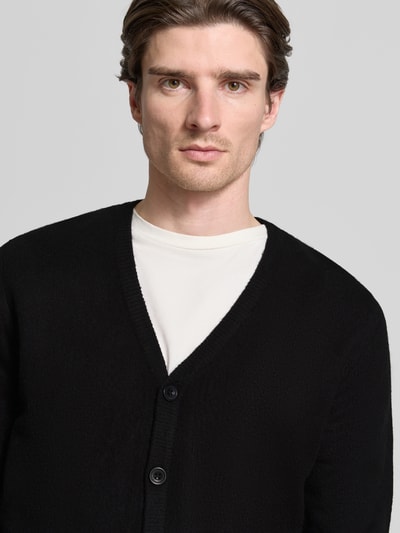 Männermodel trägt Strickjacke mit Knopfleiste Modell 'HEINE' von Casual Friday, schwarzer Material-Mix, Nahaufnahme Oberkörper.
