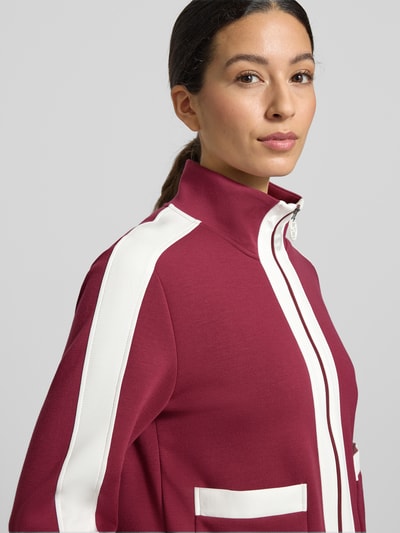 Frauenmodel trägt Regular Fit Sweatjacke mit Stehkragen von Marc Cain in Dunkelrot und Weiß, elastischer Material-Mix, Nahaufnahme Oberkörper.