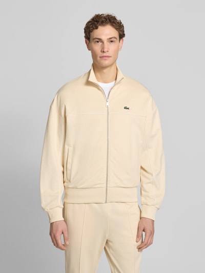 Męski model nosi Regular Fit Sweatjacke mit Baumwoll-Anteil od Lacoste, efekt: jednolity kolor, krój regular fit, zamek błyskawiczny, detal z logo, paski w kontrastowym kolorze, szew z wypustkami, stójka, długi rękaw, zakończenie rękawów i dołu prążkowane, wpuszczane kieszenie, dzianina dresowa, mieszanka materiałów z mieszanką bawełny, Ganzkörperansicht von vorne.