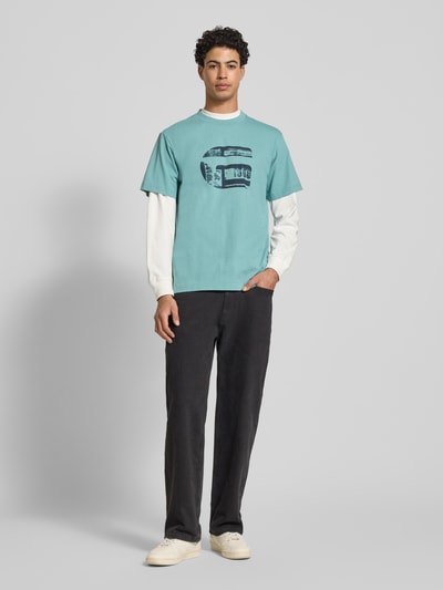 Männermodel trägt Regular Fit T-Shirt mit Logo-Print Modell 'icon' von G-Star Raw in Türkis, Baumwolle, Rundhals, Ganzkörperansicht von vorne.