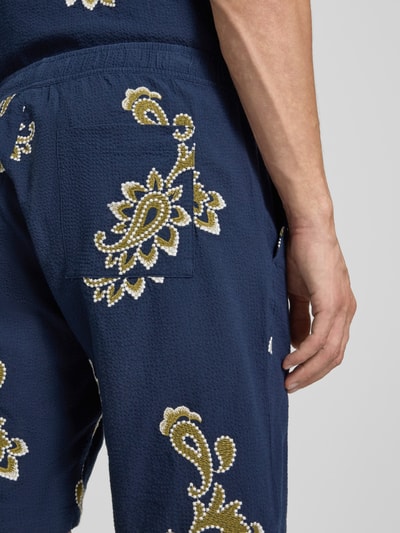 Mężczyzna nosi szorty mit Stitchings und elastischem Bund von Jake*s, mieszanka bawełny z dodatkiem streczu, krój regular fit, hafty, niebieski z żółtymi i białymi wzorami, szerokość w rozmiarze M: 41 cm, długość wewnętrzna nogawki: 22 cm, zbliżenie na tył.