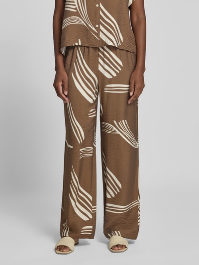 Kobiece model prezentuje Stoffhose aus Viskose-Mix Modell 'Cevil leaf' od someday., brązowy kolor z jasnym wzorem, relaxowany krój, elastyczny pas, szerokość w rozmiarze 36: 38 cm, długość nogawki od wewnątrz: 79 cm, materiał o lekko pofałdowanej teksturze, widok całej sylwetki z przodu.