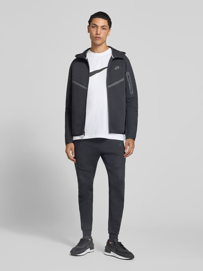 Männermodel trägt Slim Fit Sweathose aus Baumwoll-Mix von Nike in Dunkelgrau mit glatter Struktur, Ganzkörperansicht von vorne. Herren Sweathose von Nike